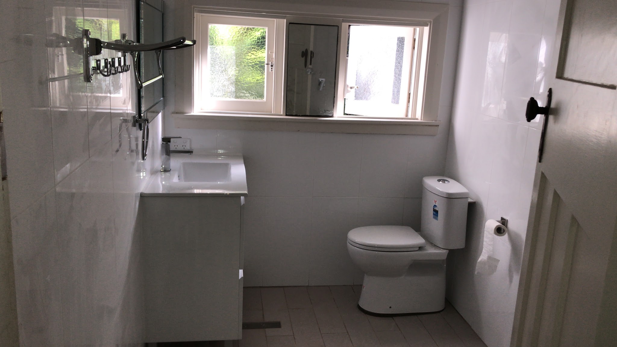 Finished bathroom with white wall tiles, a white vanity with mirror cabinet, a new toilet and a white-framed window