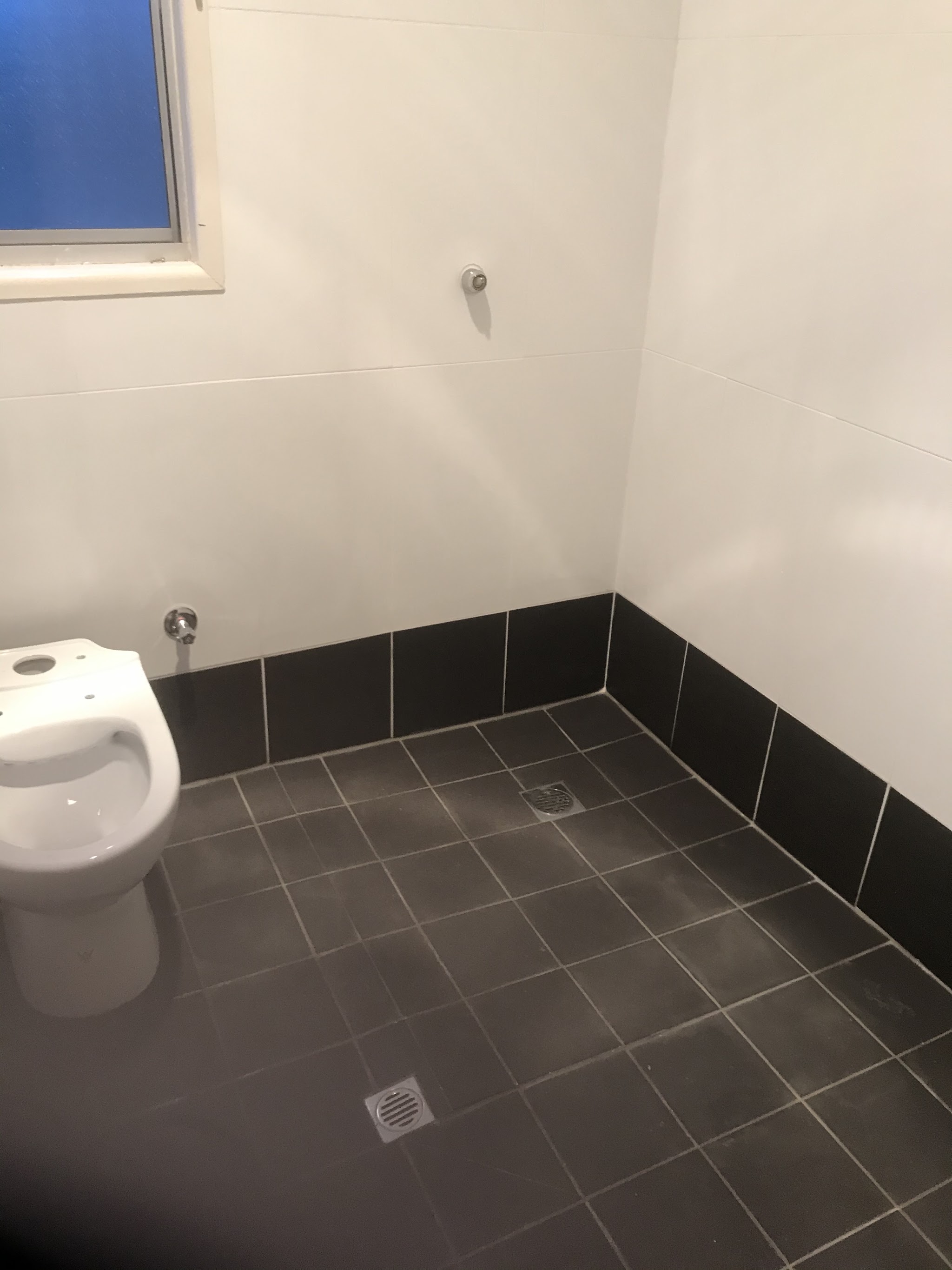 Bathroom with white walls, charcoal floor tiles, a charcoal tiled skirting row and two floor wastes
